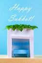 Text of Happy Sukkot. A hut made of paper covered with leaves on a blue background. Postcard, congratulations.