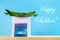 Text of Happy Sukkot. A hut made of paper covered with leaves on a blue background. Postcard, congratulations.