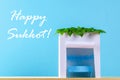 Text of Happy Sukkot. A hut made of paper covered with leaves on a blue background. Postcard, congratulations.