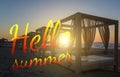 Text Hello Summer on silhouette wooden with blinds gazebo on an empty sandy beach on sunset background. Royalty Free Stock Photo