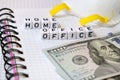 Text `Home Office`, word made of cubic letters, white protective mask and american money dollars on a white paper copybook backgr