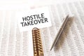 Text HOSTILE TAKEOVER on paper card, pen, financial documentation on table Royalty Free Stock Photo