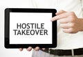 Text HOSTILE TAKEOVER on tablet display in businessman hands on the white background. Business concept