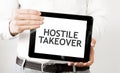 Text HOSTILE TAKEOVER on tablet display in businessman hands on the white background. Business concept