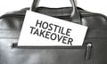 Text HOSTILE TAKEOVER writing on white paper sheet in the black business bag. Business concept