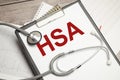 Text HSA-Health Savings Account on notebook with stethoscope and pen on wooden background Royalty Free Stock Photo