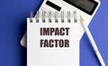 Text impact factor written on notepad with calculator and pen on blue background Royalty Free Stock Photo