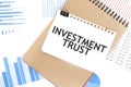 Text INVESTMENT TRUST on white paper sheet and brown paper notepad on the table with diagram. Business concept Royalty Free Stock Photo