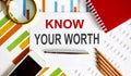 Text Know Your Worth on notepad with office tools, pen on financial report