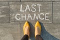 Text last chance written on gray sidewalk with women legs, top view