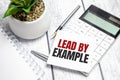 Text lead by example on paper card and calculator on wooden background Royalty Free Stock Photo