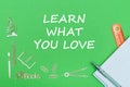 Text learn what you love, school supplies wooden miniatures, notebook with ruler, pen on green backboard