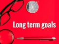 Text Long Term Goals on red background with compass,eye glasses, magnifying glass and pen.