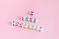 Text `Love yourself` made out of square beads on pastel pink background