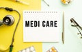 Text MEDI CARE on notebook with stethoscope and pen on yellow background