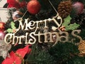 Text of Merry Christmas accessory hanging on Xmas tree closeup. Preparing & decorating Christmas tree with Xmas ornament.