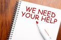 Text we need your help written in notepad, Office wood table and red marker from above, concept image for blog title or header Royalty Free Stock Photo