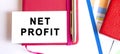 Text NET PROFIT on white card lying on notepad on office desk. Financial concept