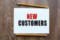 The text NEW CUSTOMERS is written in a notebook which lies on a wooden table. Lettering on a business or financial theme. Business