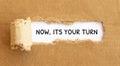 Text Now, Its Your Turn appearing behind torn brown paper