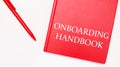 The text ONBOARDING HANDBOOK is written on a red notepad near a red pen on a white table in the office. Business concept Royalty Free Stock Photo