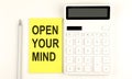 Text OPEN YOUR MIND on yellow sticker, next to pen and calculator