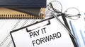 Text PAY IT FORWARD on Office desk table with notebooks, supplies,analysis chart, on the white background. Top view Royalty Free Stock Photo