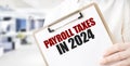 Text PAYROLL TAXES IN 2024 on white paper plate in businessman hands in office. Business concept
