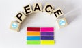 The text PEASE is written on wooden blocks, on a white background. The colors of the rainbow as stickers lie side by side