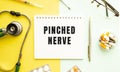 Text PINCHED NERVE on notebook with stethoscope and pen on yellow background.