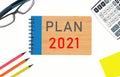 the text of plan 2021 on a notepad on a light background next to pencils, glasses, a calculator and writing paper. Royalty Free Stock Photo