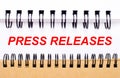 Text PRESS RELEASES on white paper between white and brown spiral notepads