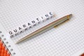 Text `Quarantine`, word made of cubic letters and luxury pen on a white paper note pad background. Royalty Free Stock Photo