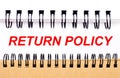 Text RETURN POLICY on white paper between white and brown spiral notepads