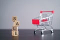Text `SALE` on wooden cube with shopping cart over background