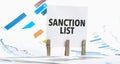 Text sanction list on paper sheet with chart, dice, spectacles, pen, laptop and blue and yellow push pin on wooden table Royalty Free Stock Photo