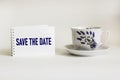 Text Save the date written on notepad and white background with beautiful cup next to it Royalty Free Stock Photo