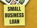 Text SMALL BUSINESS LOAN written on yellow paper note on calculator.