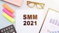 The text SMM 2021 - SOCIAL MEDIA MARKETING on office desk with calculator, markers, glasses and financial charts