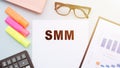 The text SMM - SOCIAL MEDIA MARKETINGon office desk with calculator, markers, glasses and financial charts