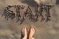 Text start written in sand on sea beach and womans bare feet