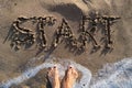 Text start written in sand on sea beach and womans bare feet