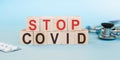 Text STOP COVID-19 on wooden cubes on blue background with tablets and stethoscope. Stop the global coronavirus pandemic