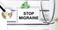 Text Stop Migraine in a notebook on medical forms with a phonendoscope and green pills Royalty Free Stock Photo