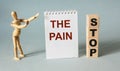 The text Stop Pain is written on a notebook and wooden cubes, next to a wooden person on a light blue background.