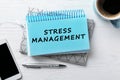 Text Stress Management in notebook on white wooden table with phone and cup of coffee, flat lay Royalty Free Stock Photo