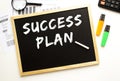 Text SUCCESS PLAN written in chalk on a slate board. Office desk with office supplies Royalty Free Stock Photo