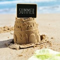 Text summer in a signboard topping a sandcastle