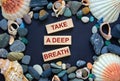 Text `take a deep breath` on wooden blocks on a beautiful black background. Sea stones and seashells. Concept