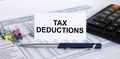 Text Tax Deductions on white card with blue metal pen, calculator and paper clips on financial table